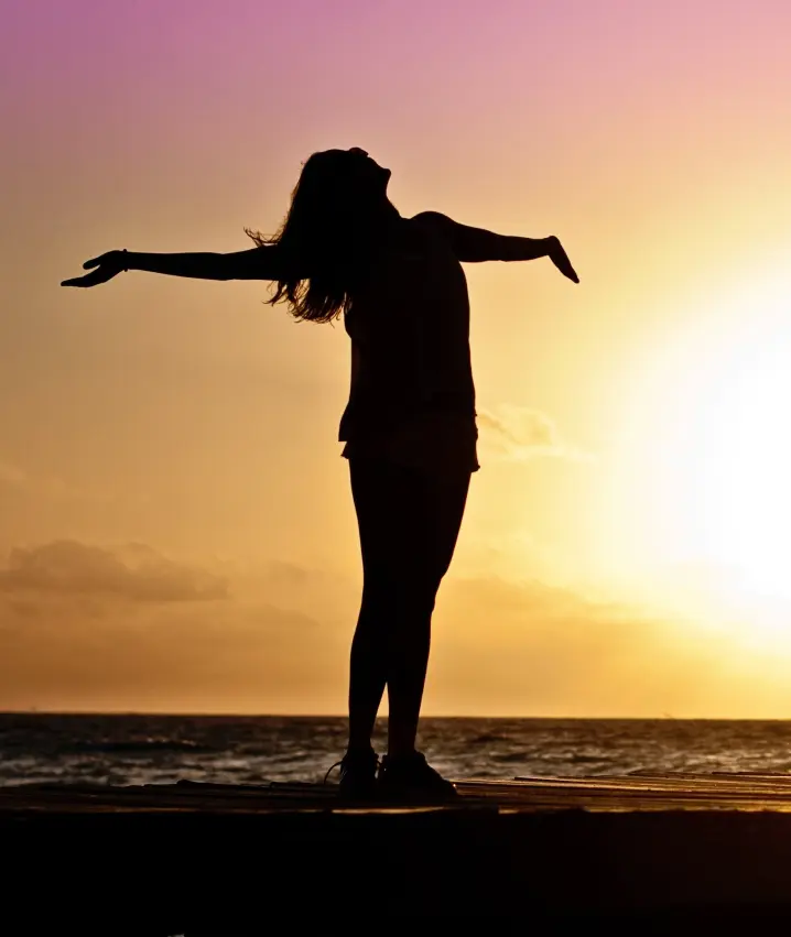 A silhouette of a woman with her arms outstretched at sunset.