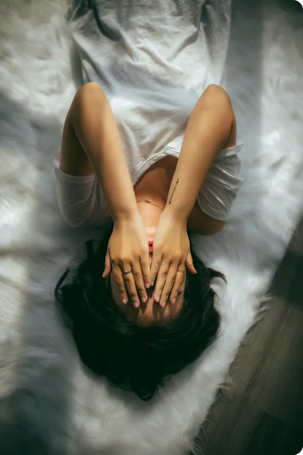A woman laying on a bed with her hands on her face.