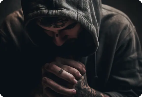 A man in a hoodie praying with his hands on his knees.