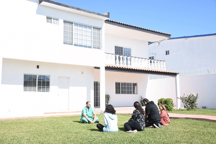 A group of people sitting on the grass in front of a house.