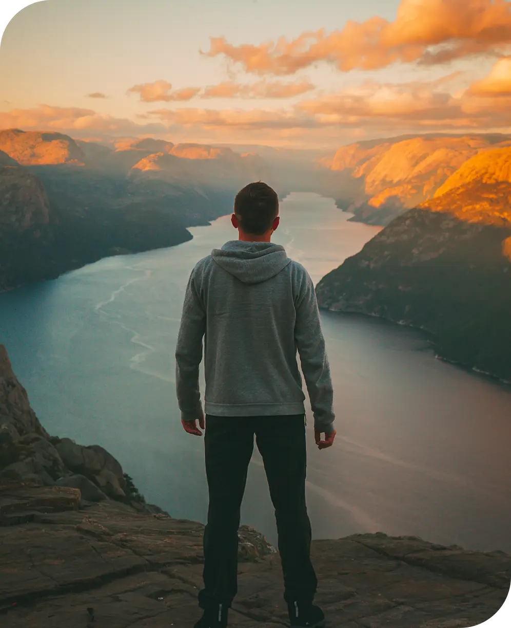 A man standing on top of a mountain overlooking a lake.