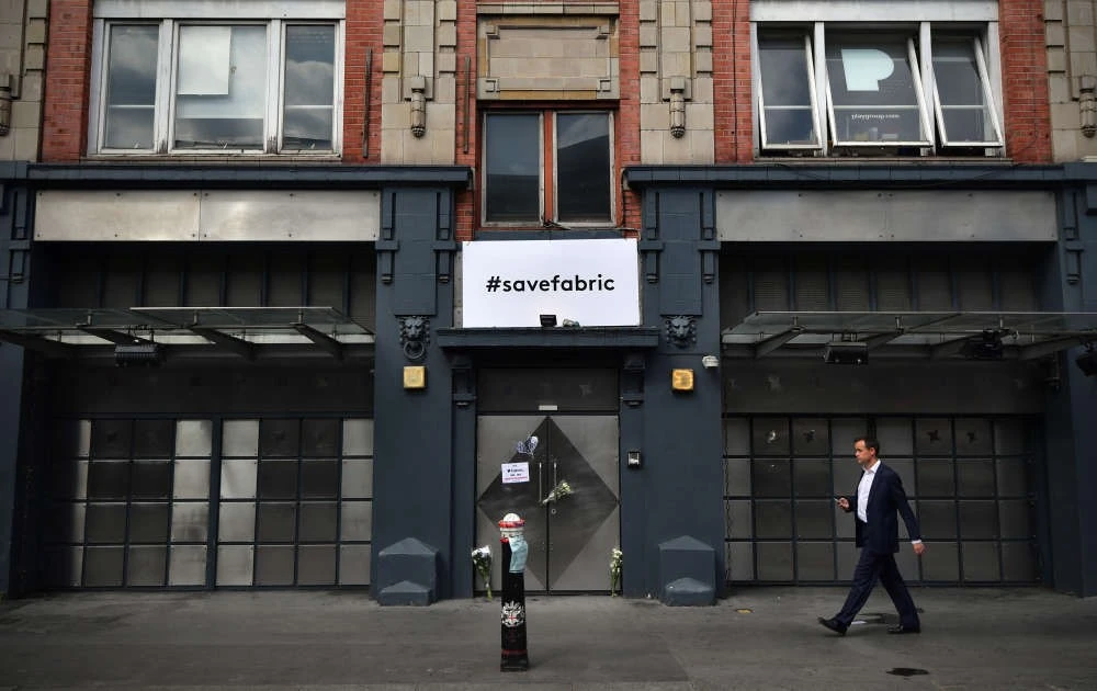 Man walking past building with "#savefabric" banner.
