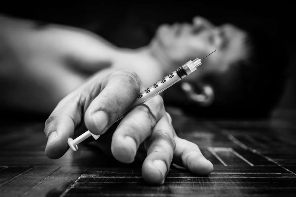 Man unconscious with syringe in hand, black and white.