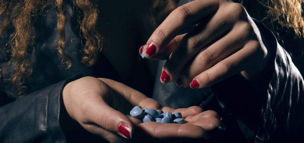 Woman holding pills in dimly lit setting.